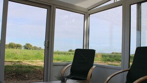 Una habitación con dos sillas verdes, una mesa pequeña y vistas a un campo cubierto de césped a través de ventanas amplias.