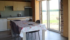 Una cocina con armarios de madera, una mesa de comedor con sillas y un amplio ventanal corredero que da a un espacio exterior.