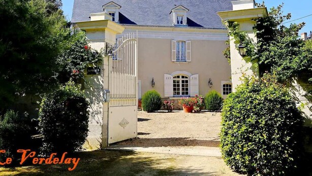 A two-story building with a gated entrance, a small balcony on the upper floor, and a garden area with potted plants. - Elegant B&B in La Ménitré with heated pool and wifi (La Ménitré)