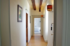 Un couloir doté d’un plancher en bois, de murs blancs et d’une porte donnant sur une salle de bain avec une baignoire.