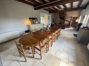 A spacious dining area with a long wooden table and chairs, a radiator, and a staircase leading to an upper level.