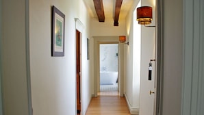 A hallway with wooden flooring, white walls, and a door leading to a bathroom with a bathtub.