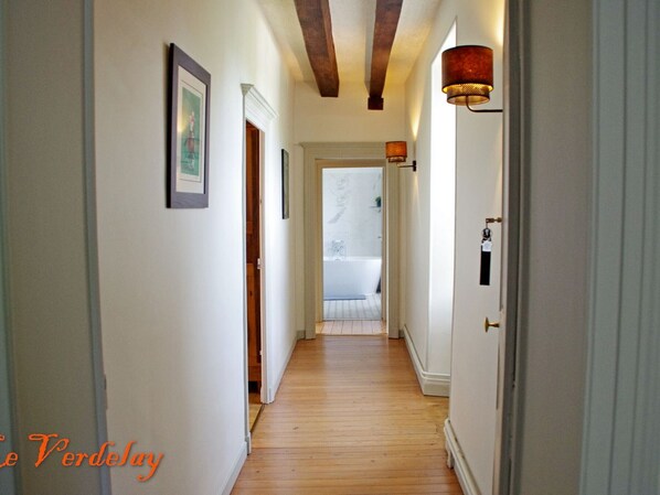A hallway with wooden flooring, white walls, and a door leading to a bathroom with a bathtub.