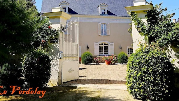 A two-story building with a gated entrance, a small balcony on the upper floor, and a garden area with potted plants.