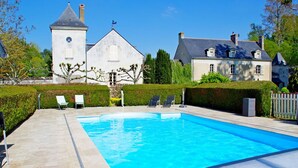 A swimming pool with lounge chairs, a white building with a clock tower, and another house with a sloped roof.