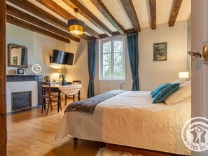 Un dormitorio con cama, escritorio, silla, televisor y ventana con cortinas.