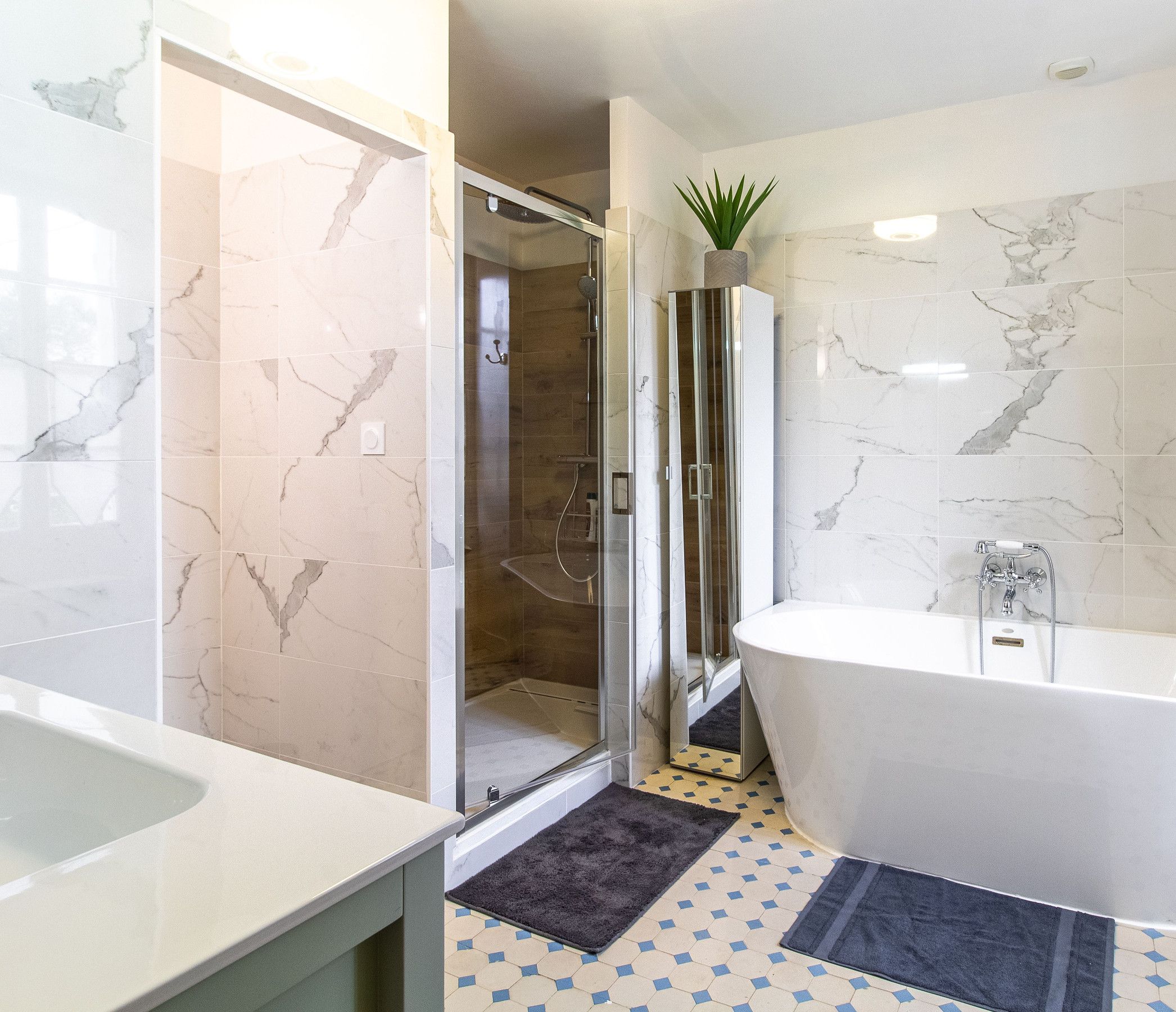 Ein modernes Badezimmer mit barrierefreier Dusche, einer freistehenden Badewanne und einem durch eine Glaswand abgetrennten Duschbereich.