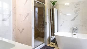 Ein modernes Badezimmer mit barrierefreier Dusche, einer freistehenden Badewanne und einem durch eine Glaswand abgetrennten Duschbereich.