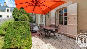 Un patio con una mesa y sillas bajo un paraguas naranja, una puerta blanca y un suelo de losas de piedra.
