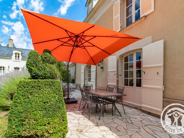 Un patio con una mesa y sillas bajo un paraguas naranja, una puerta blanca y un suelo de losas de piedra.