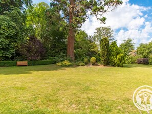 A well-maintained garden with a wooden bench, various trees, and a clear sky. - Elegant B&B near Loire with park and pool (La Ménitré)
