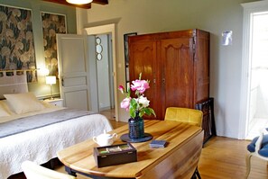 Habitación de hotel con una cama, una mesa de madera con un florero y una silla, además de un armario.