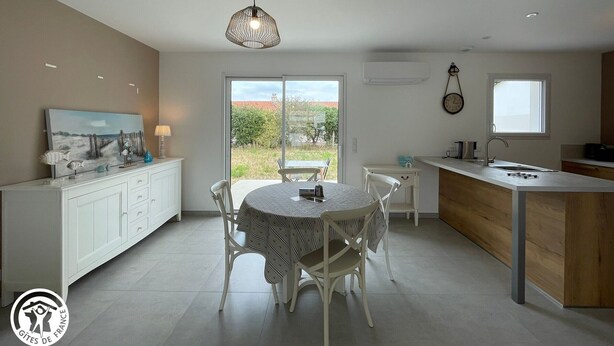 Una cocina moderna con comedor, que cuenta con un ventanal grande, una lámpara colgante y un reloj en la pared.