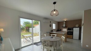 Una cocina moderna con comedor, que incluye una puerta corrediza de vidrio a un jardín, una isla central y una lámpara colgante.