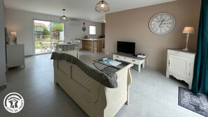 Una sala de estar moderna con sofá, mesa de comedor, televisor y zona de cocina.