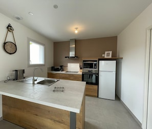 A modern kitchen with a central island, a built-in oven, microwave, and refrigerator.