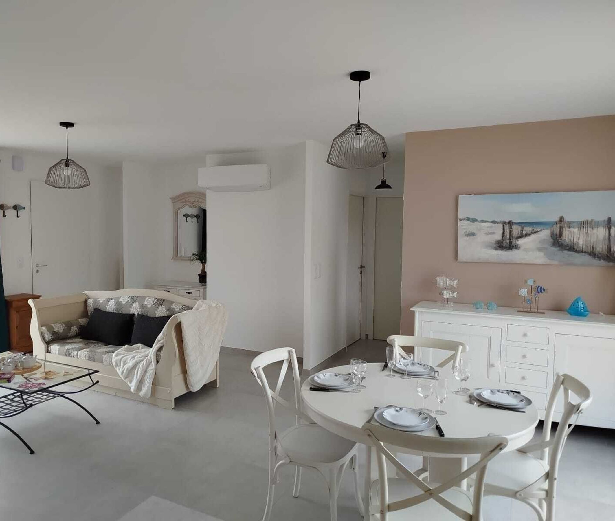 A modern, well-lit room with a bed, a dining table set for two, and a painting on the wall.