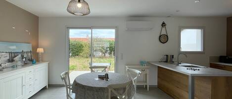 A modern kitchen with a dining area, featuring a large window, a pendant light, and a clock on the wall.