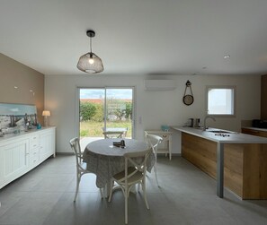 A modern kitchen with a dining area, featuring a large window, a pendant light, and a clock on the wall.