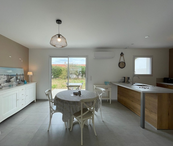 A modern kitchen with a dining area, featuring a large window, a pendant light, and a clock on the wall.
