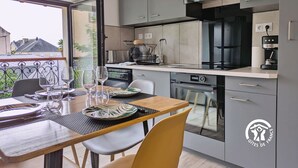 A modern kitchen with grey cabinets, a black stove, and a coffee machine. There is a dining area with a table and chairs. - Cozy apartment in Laval, parking included, for 4 people (Laval)