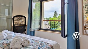 A hotel room with a bed, a chair, a window with curtains, and a view of greenery outside. - Cozy apartment in Laval, parking included, for 4 people (Laval)