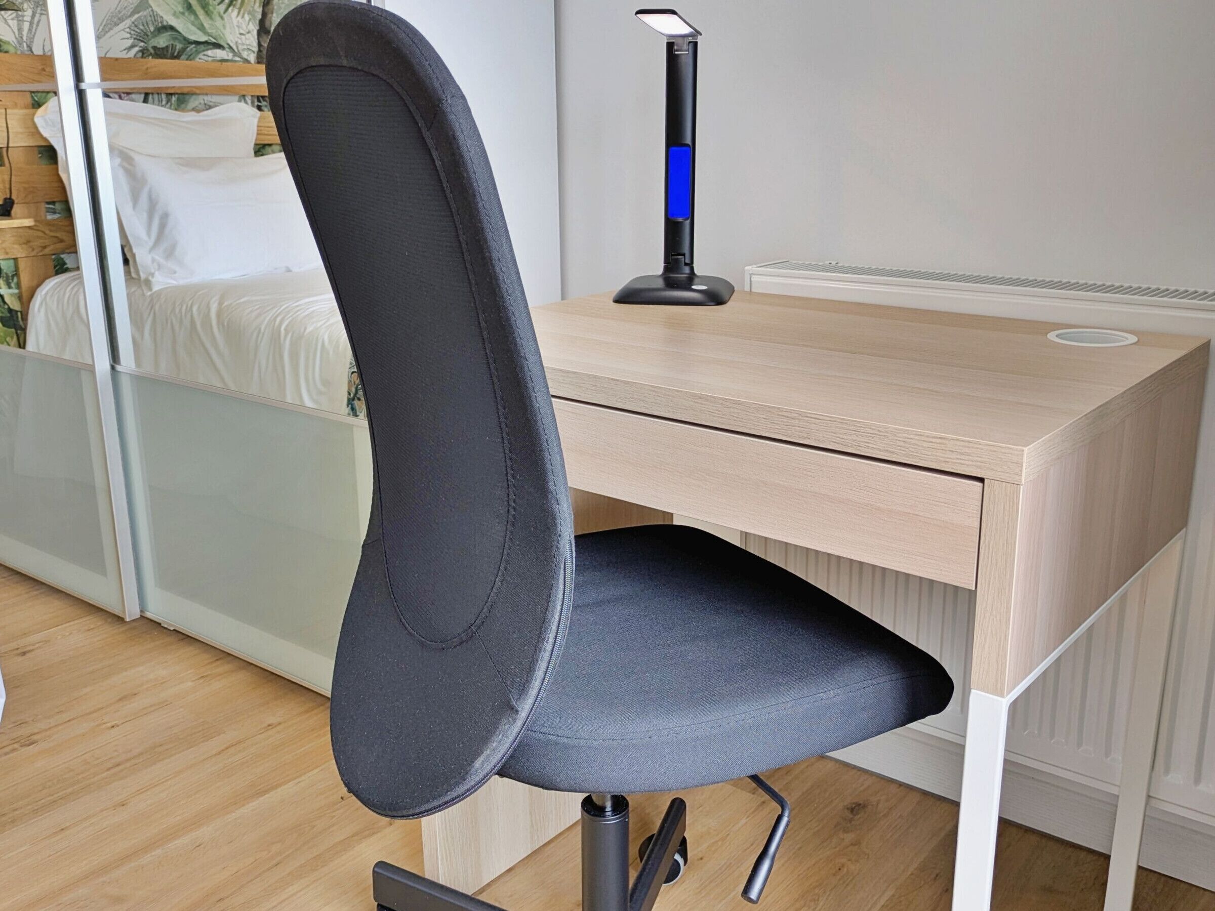 Una silla de oficina moderna con respaldo alto y asiento acolchado, ubicada frente a un escritorio de madera con soporte incorporado para monitor.