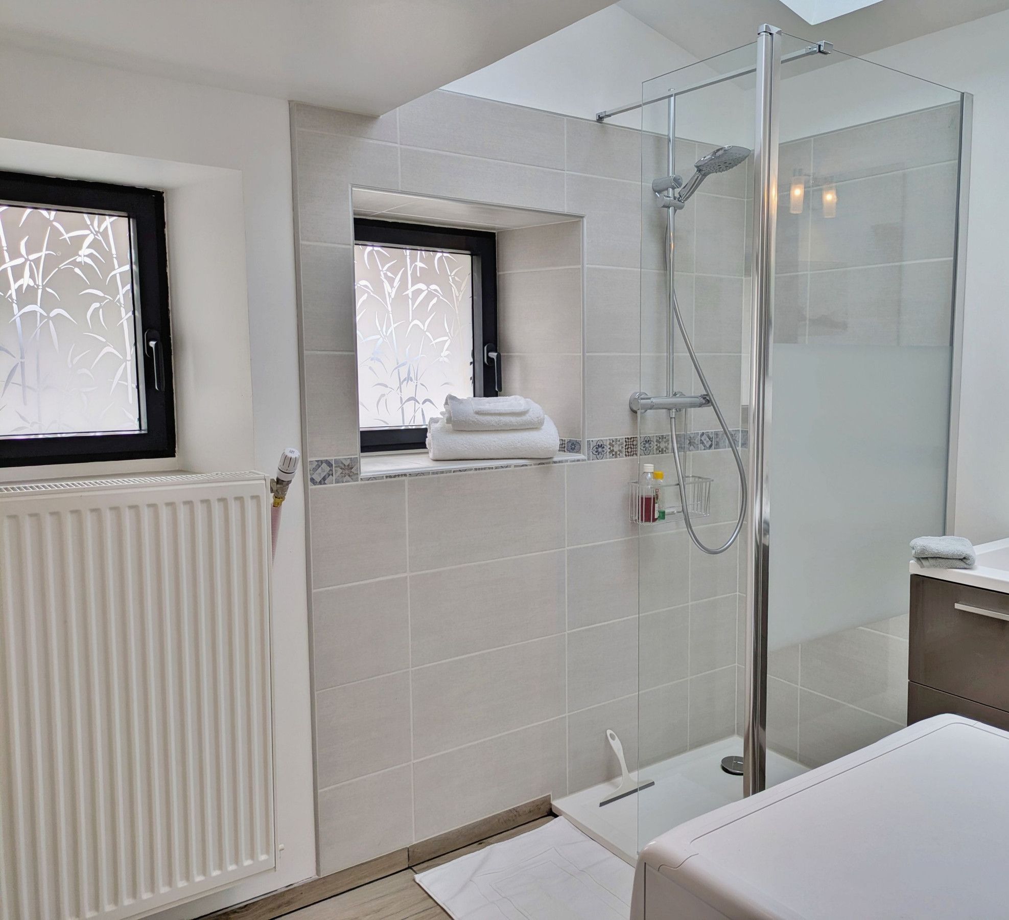 A modern bathroom with a glass-enclosed shower, a white sink, and a window with a view of bamboo.