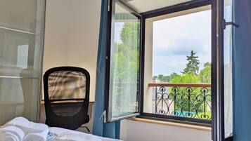 A hotel room with a bed, a chair, a window with curtains, and a view of greenery outside.