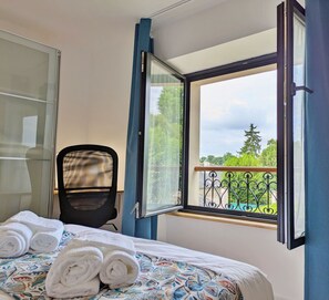 Ein Hotelzimmer mit einem Bett, einem Sessel, einem Fenster mit Vorhängen und Blick auf Grünfläche.