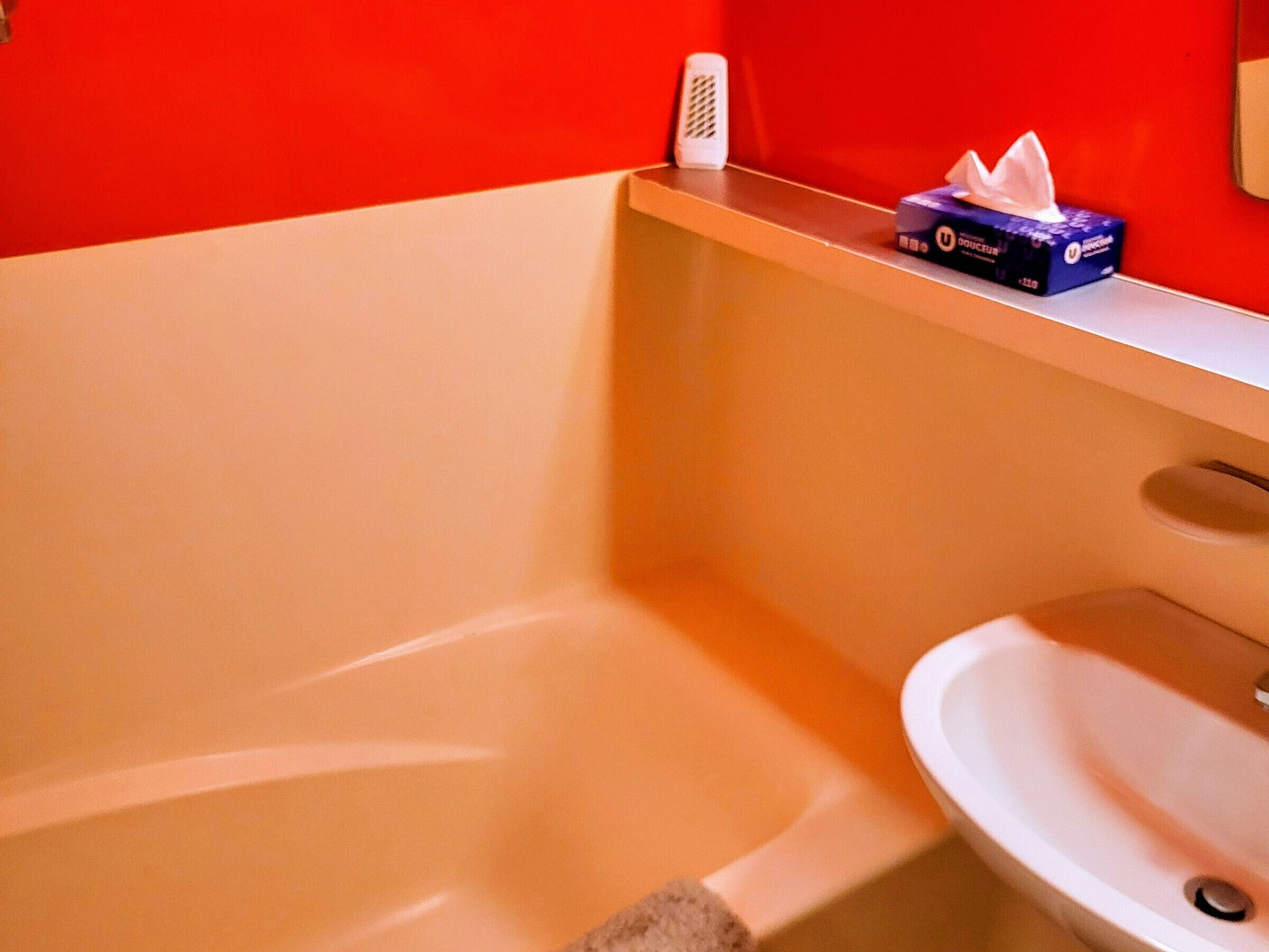 Een badkamer met een witte wastafel, een spiegel en een zakdoekendoosje op het aanrecht.