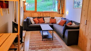 A cozy living room with a sectional sofa, a coffee table, and a view of a forest through large windows. - Apartment 5 pers, Bright, Wifi, Pets allowed (Les Arcs 1800)