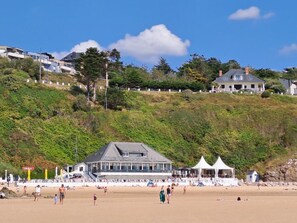 A beach with a building with a large balcony overlooking the sea, a white tent, and people on the sand. - Holiday Home 3 BR, Private Garden, Beach 100m Away (Saint-Jean-de-la-Rivière)