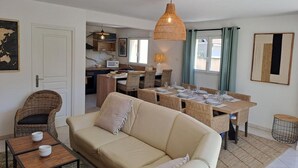 Ein gemütliches Wohnzimmer mit einer Couch, einem Esstisch für vier Personen und einer Küche im Hintergrund.