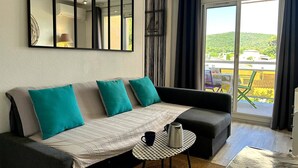 A modern living room with a sofa, a coffee table, and a large window with a view of greenery.