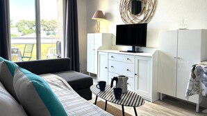 A modern living room with a sofa, a small table with cups, a television on a cabinet, and a large window with curtains.