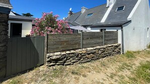 Una propiedad residencial con un muro de piedra, una valla de madera y una casa con techo gris y antena parabólica.
