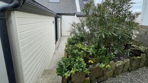 Un edificio residencial con puerta de garaje, antena parabólica y jardín con diversas plantas y un muro de piedra.