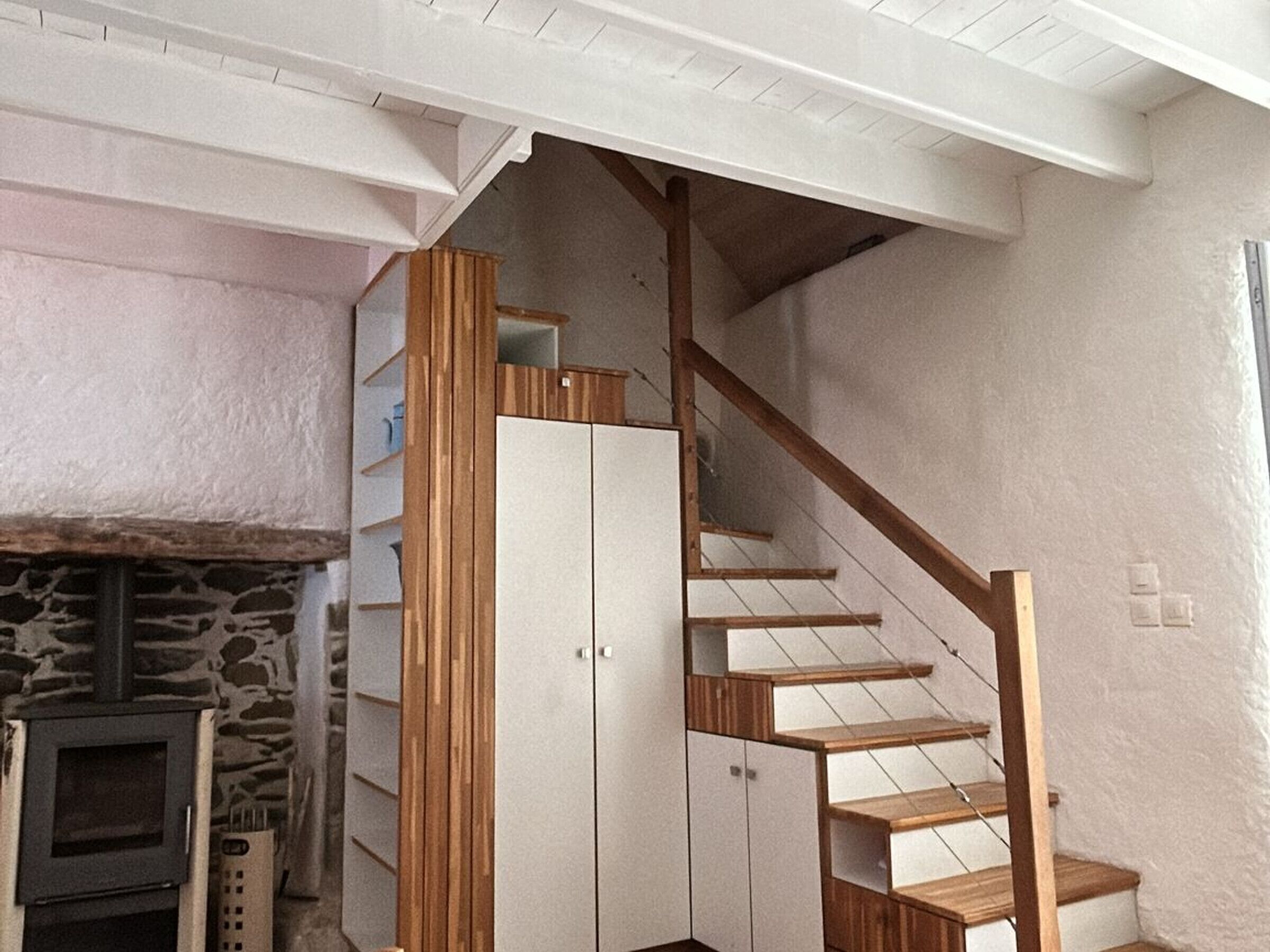 A staircase with wooden steps and white walls, leading to a landing with a stone fireplace.