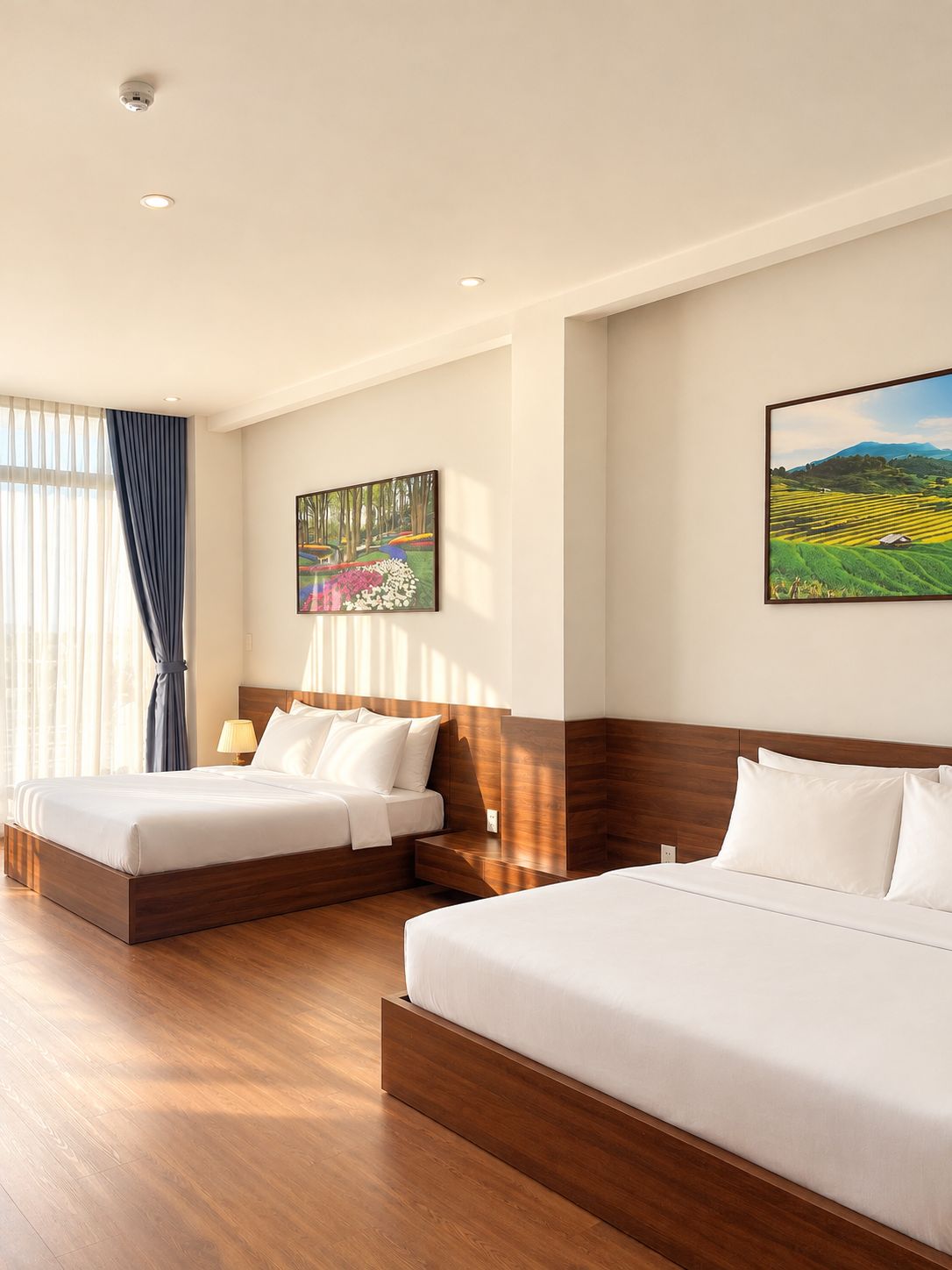 Une chambre d’hôtel avec deux lits, un tableau représentant une forêt, un tableau représentant un paysage et une fenêtre avec des rideaux.