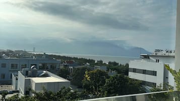 Blick von einem Balkon auf eine Stadtlandschaft mit Gebäuden, einem Gewässer und Bergen im Hintergrund.