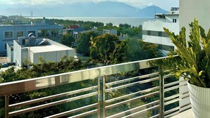 Ein Balkon mit Metallgeländer, einem Blumentopf und Blick auf Gebäude sowie einen entfernten Berg.