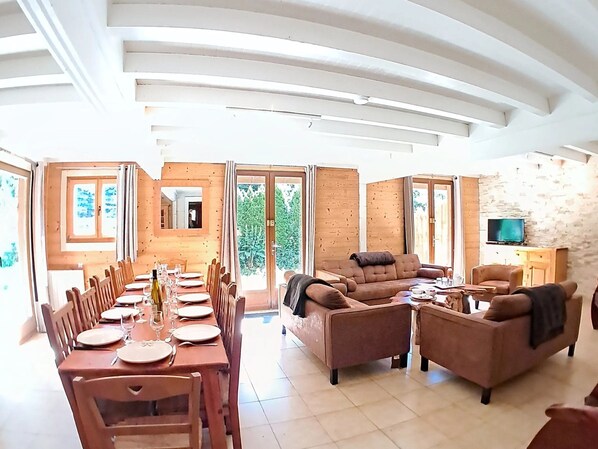 Amplia sala de estar con una mesa de comedor lista para una comida, un sofá y un televisor.