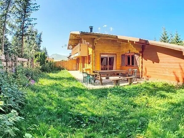 A wooden cabin with a patio, surrounded by lush greenery and trees.
