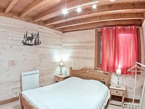A wooden cabin bedroom with a bed, bedside tables, a lamp, a mirror, and a red curtain.