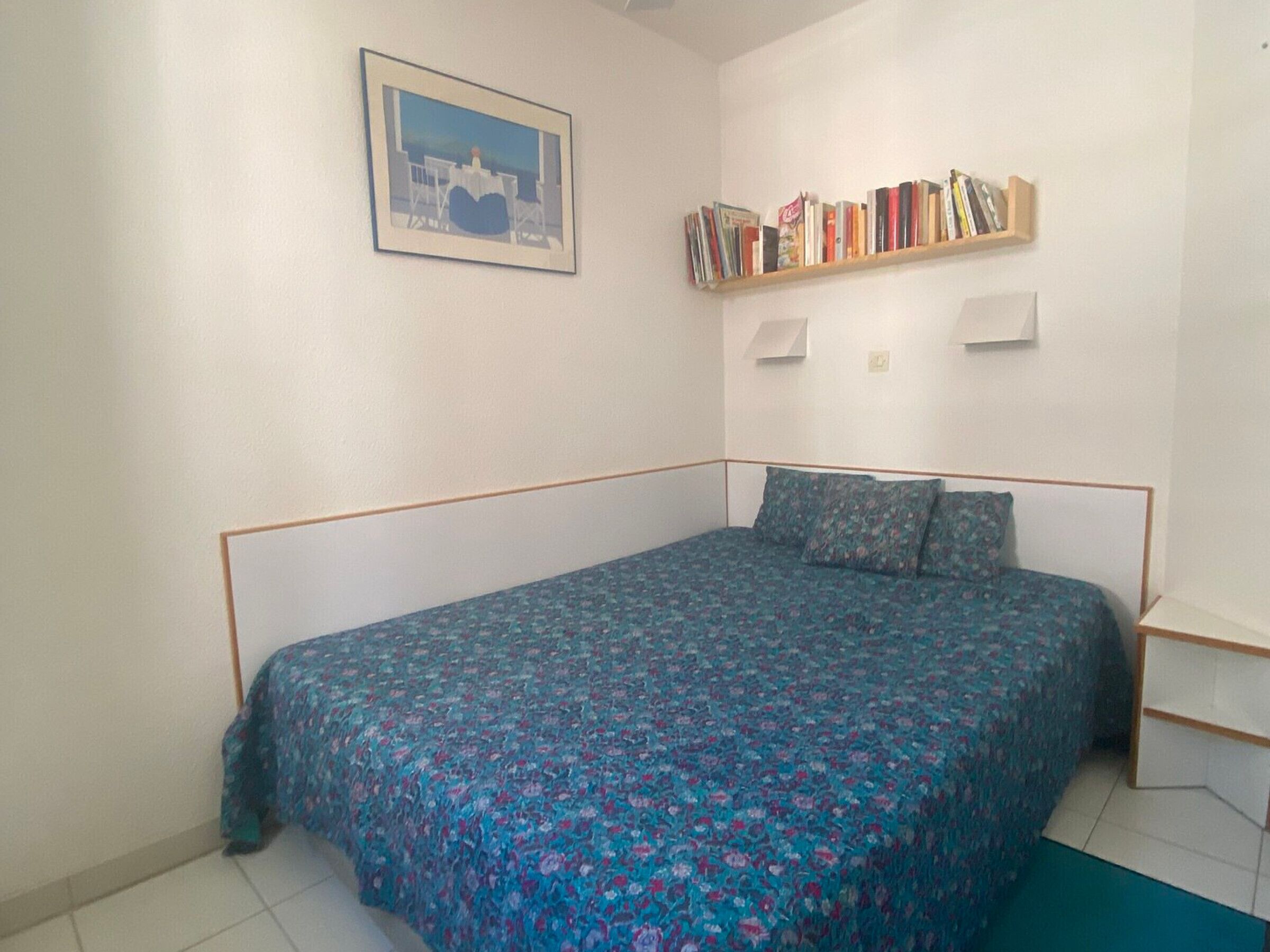 A bedroom with a bed, a bookshelf, and a framed picture on the wall.
