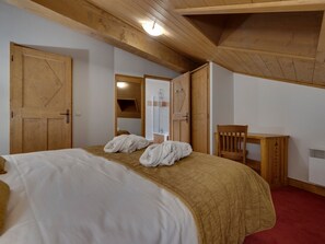 A bedroom with a bed, a wooden desk, a chair, and a bathroom with a shower.