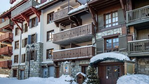 A multi-story hotel with stone and wood exterior, balconies, and a snow-covered entrance. - Arc 1950 - 3-Room Apartment, 67sqm, 6 pax (Les Arcs 1950)