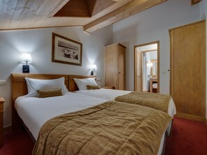 A hotel room with two beds, wooden headboards, a framed picture on the wall, and a wardrobe.