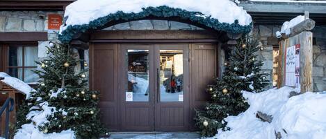A snow-covered entrance to a building with two Christmas trees and a sign indicating a residence for tourism.
